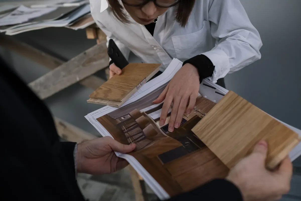 두 명의 전문가가 인테리어 디자인을 위해 목재 샘플과 디자인 프린트를 검토하며 협력하는 모습