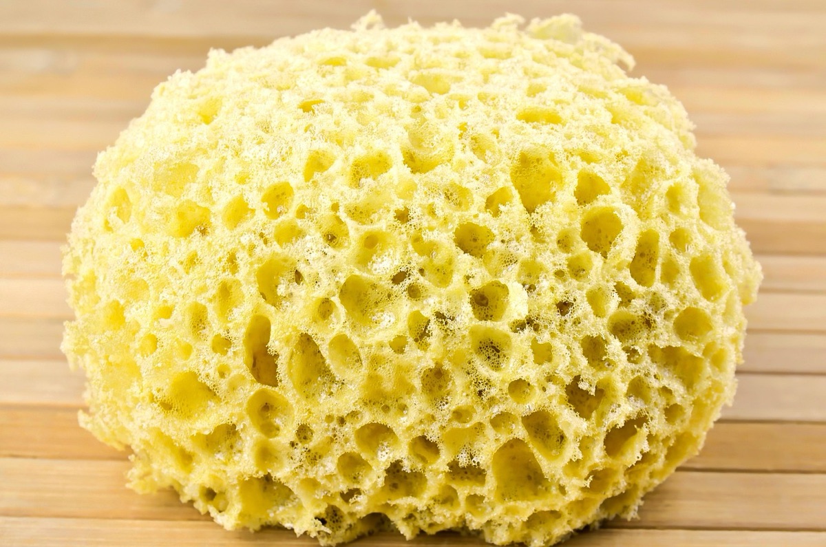 A person's hands using a yellow sponge to scrub a white ceramic sink basin.
