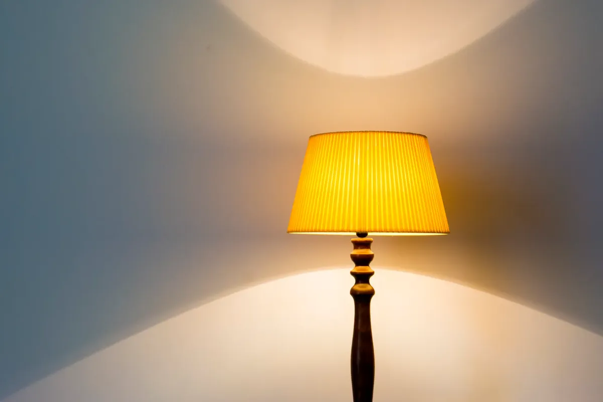 A classic table lamp with a textured yellow lampshade against a white wall casting soft shadows.